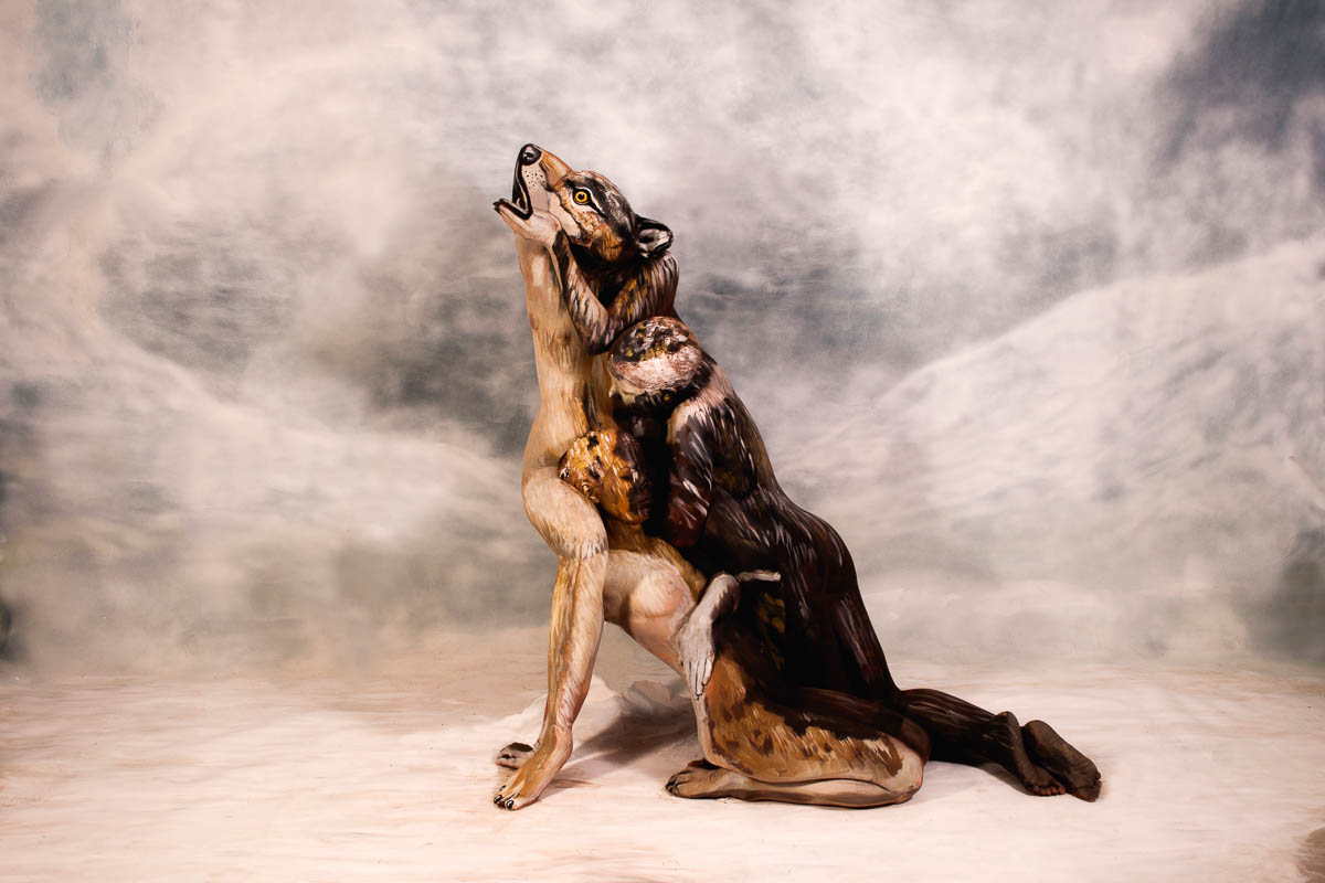 Zwei kunstvoll bemalte Körper formen gemeinsam die Illusion eines heulenden Wolfs, meisterhaft verschmolzen durch Bodypainting in einer winterlichen Landschaft.