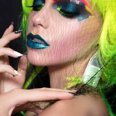 Close-up of a model with neon green hair, bold colorful eye makeup, and a black net veil over the face.