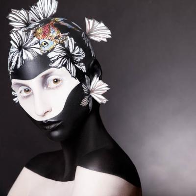 Portrait of a model with black and white body paint, floral designs on the head, and a small painted fish detail.