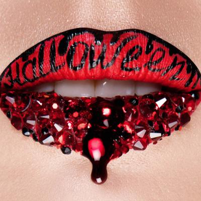Close-up of red lips with black lettering and red crystals, dripping red liquid.