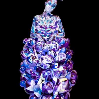 Performer with full-body paint and a sculptural purple balloon dress, posing against a black background.