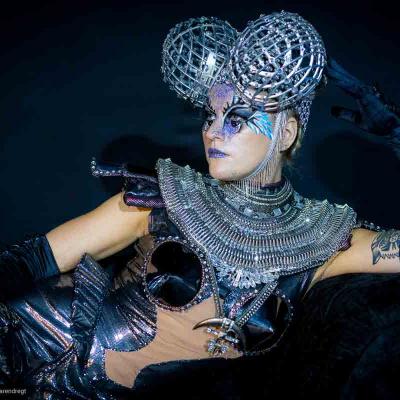 Person in silver futuristic costume with spherical metallic headpiece posing against a dark background.
