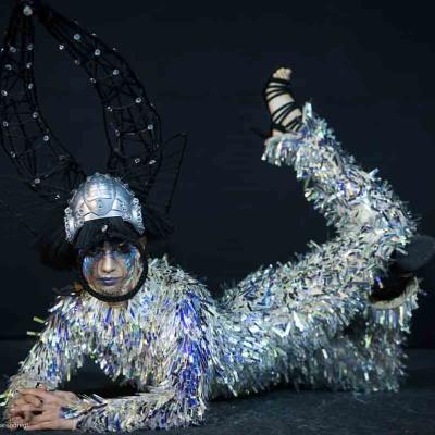 Person in silver tinsel costume with large black rabbit ears lying against a dark background.