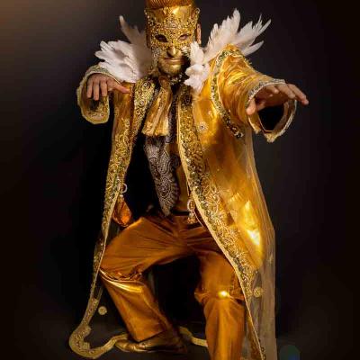 Performer in an ornate gold costume and mask posing dramatically against a dark background.