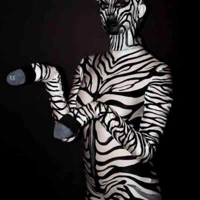 Person painted like a zebra with black and white stripes and ears, posing against a dark background.