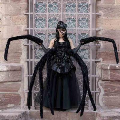 Person in a black spider-inspired costume with multiple long legs, standing in front of a stone building.