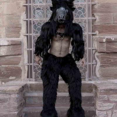 Person wearing a black horned animal costume standing on stone steps in front of a stone building.